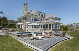 The exterior of a modern coastal home near Newport with an infinity pool, deck, and built in grill