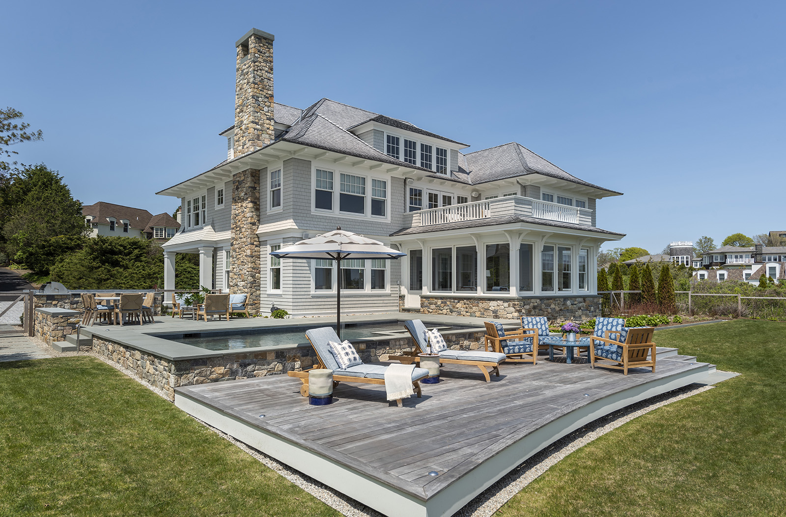 The exterior of a modern coastal home near Newport with an infinity pool, deck, and built in grill