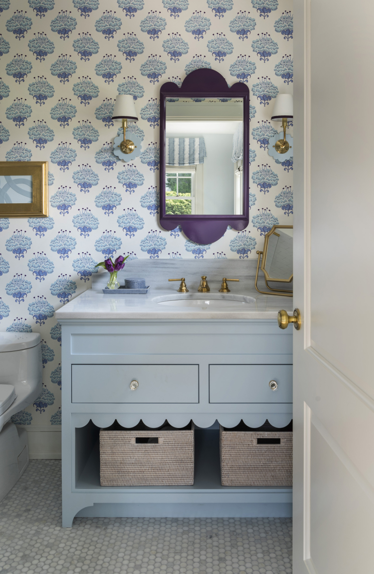 A lavender, blue and white guest bathroom with a blue mirror and vanity with scallop edge in a modern coastal home designed by Taste Interior Design