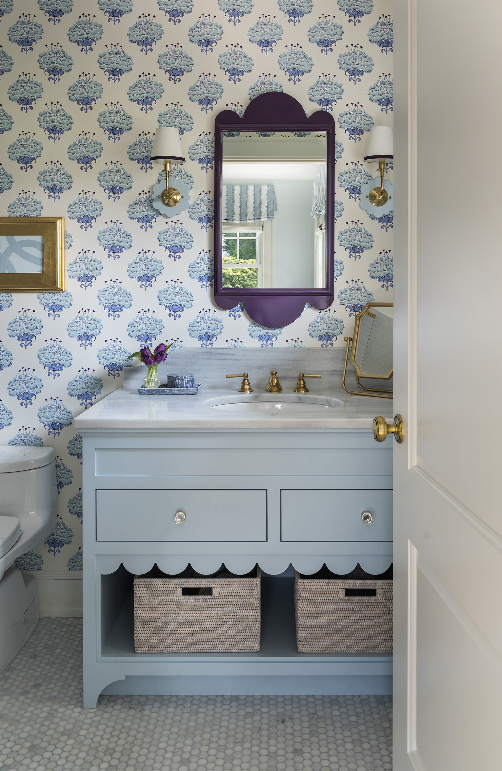 A lavender, blue and white guest bathroom with a blue mirror and vanity with scallop edge in a modern coastal home designed by Taste Interior Design