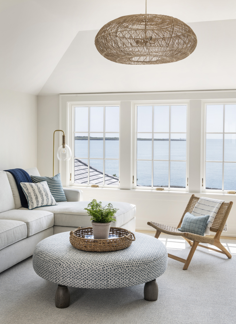 A neutral coastal sitting room with an upholstered ottoman and rattan light fixture in a modern coastal home designed by Taste Interior Design