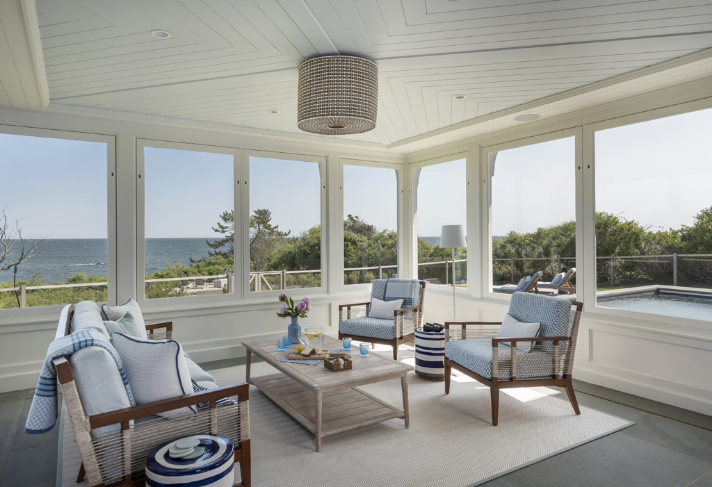 A three season room with a Serena and Lily pendant light and Palecek outdoor sofa in a modern coastal home on the New England Coast