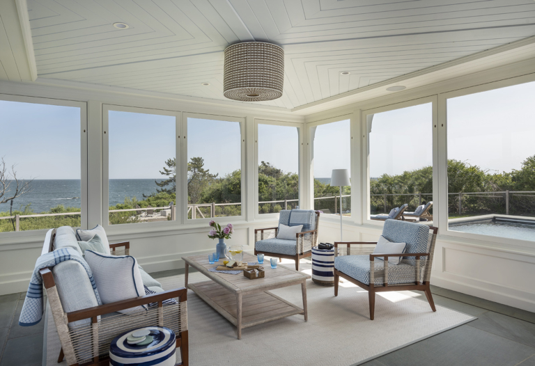A three season room with a Serena and Lily pendant light and Palecek outdoor sofa in a modern coastal home on the New England Coast