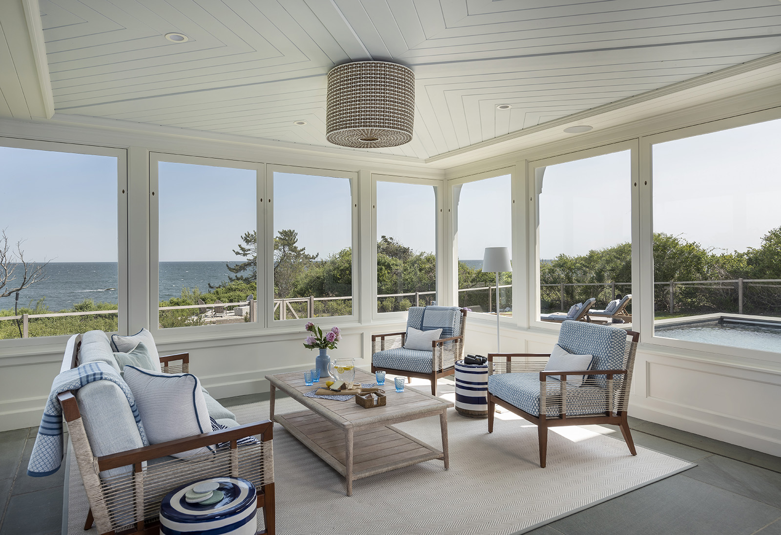 A three season room with a Serena and Lily pendant light and Palecek outdoor sofa in a modern coastal home on the New England Coast