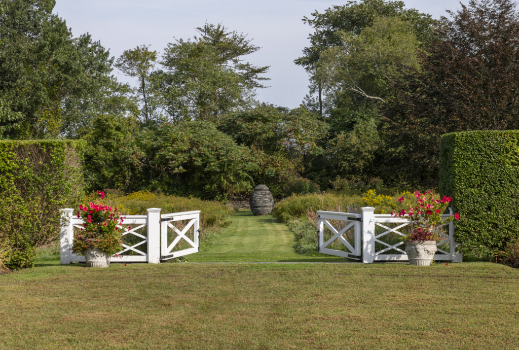 A garden with a white gate opening to a cairn