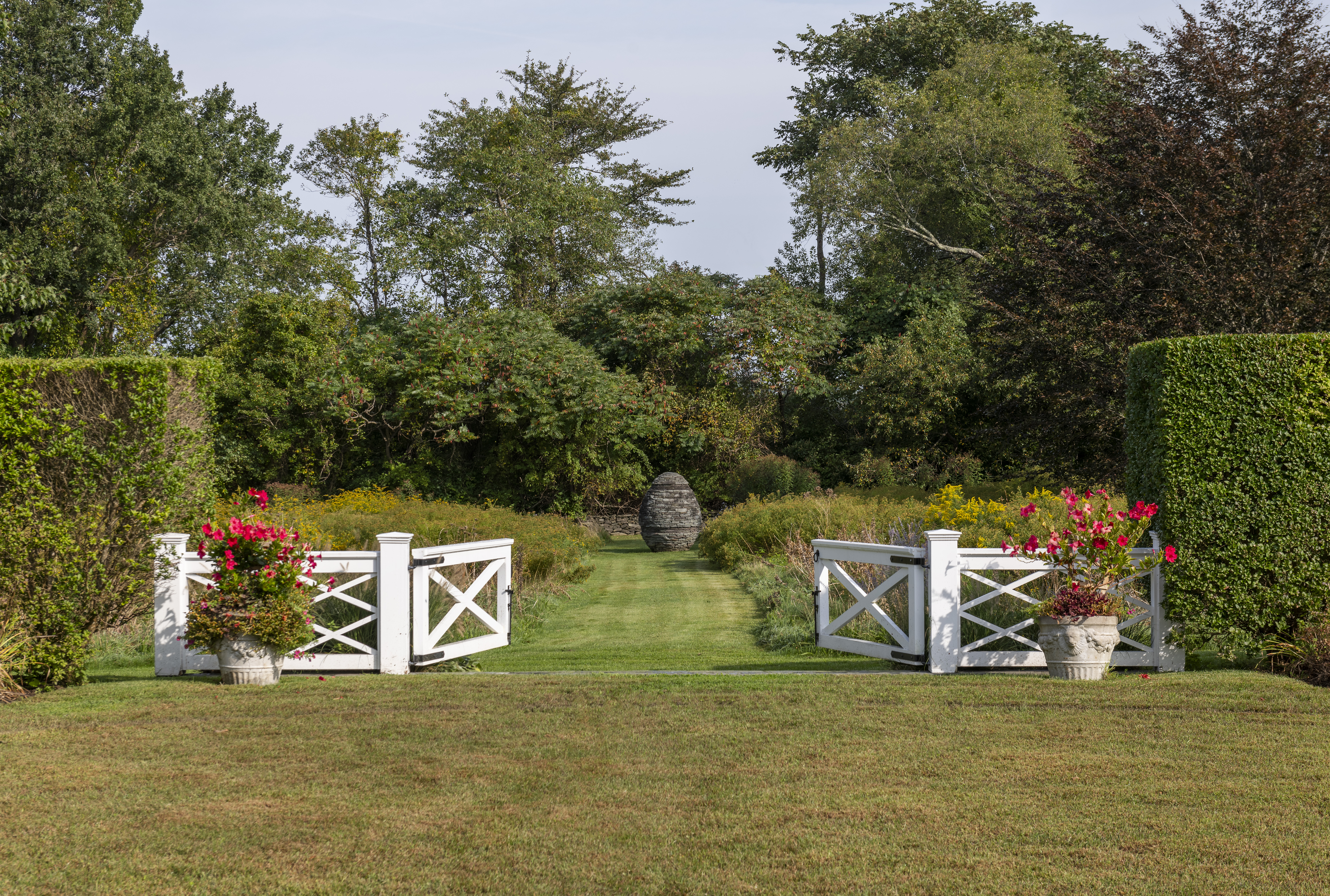 A garden with a white gate opening to a cairn
