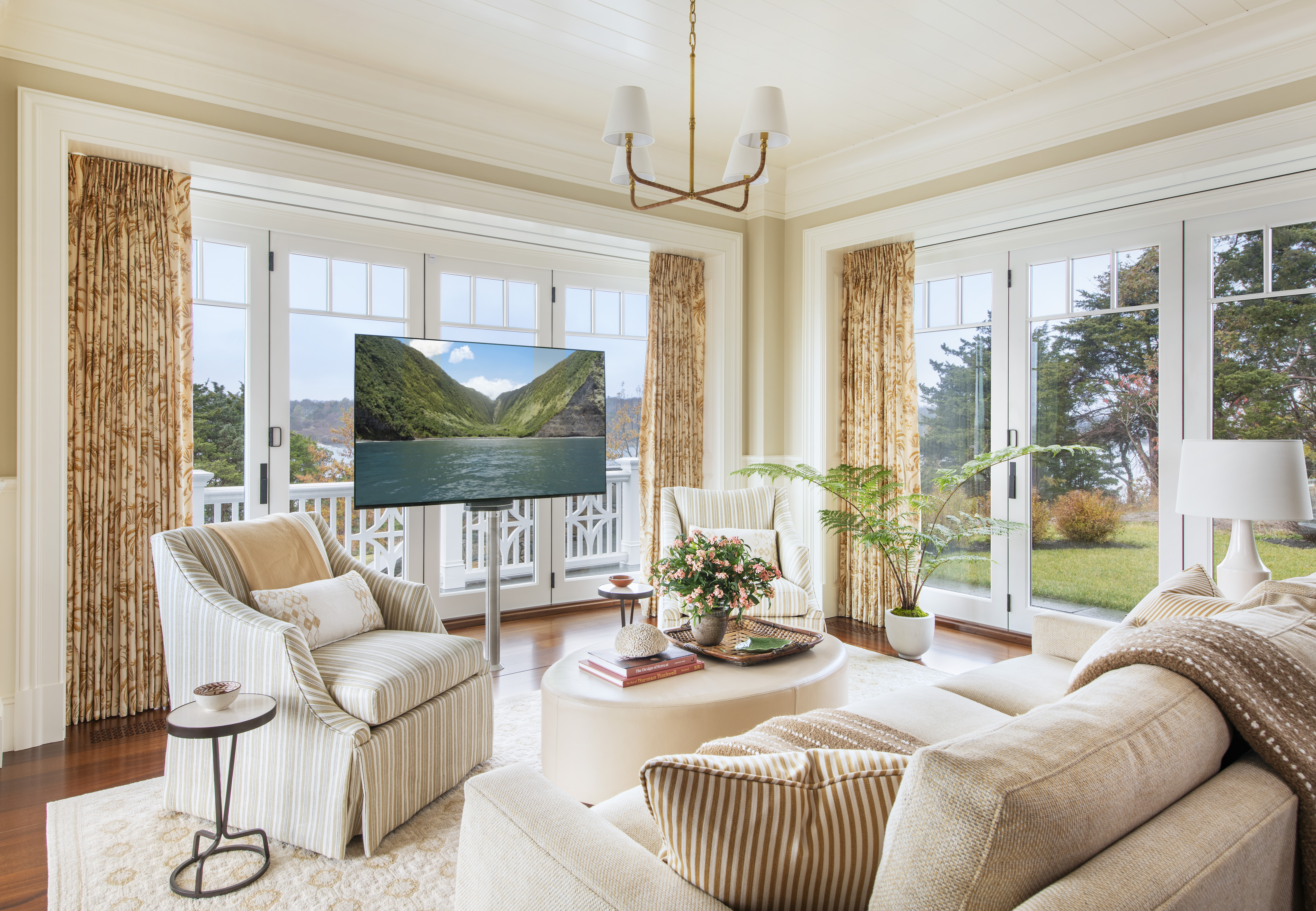 A buttery yellow family room in a coastal summer home with a tv raised from the floor on a lift.