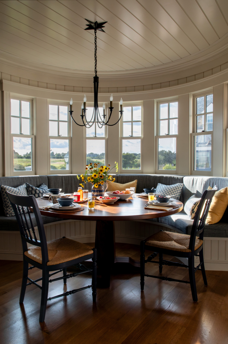 Curved bay window breakfast nook with built-in bench seating, a round wood table, and morning sunlight illuminating a casually set table at Ocean Lodge.