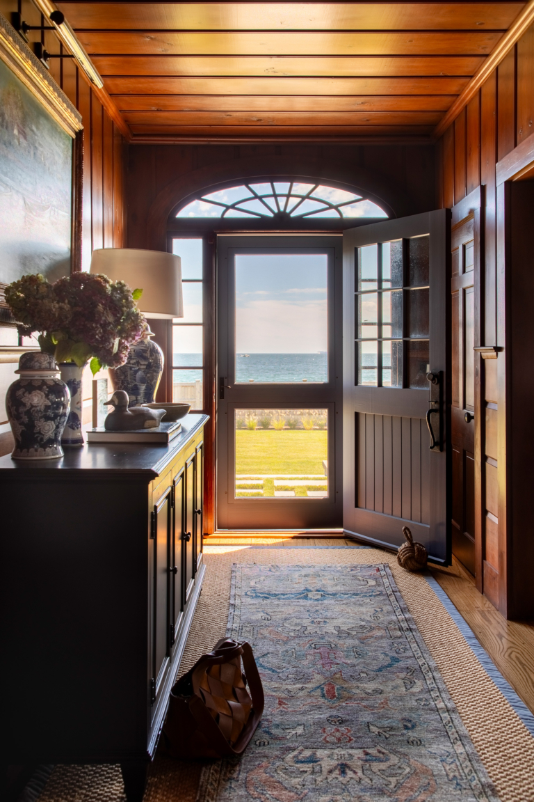 View from the front entry hall through to the ocean, framed by original wood paneling, custom millwork, and a Dutch door at Ocean Lodge.