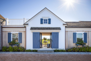 Front entry view of Ocean Lodge in Newport, showcasing restored architecture with blue shutters, vertical wood siding, and historic detailing by Taste Design Inc. and Patrick Ahearn.