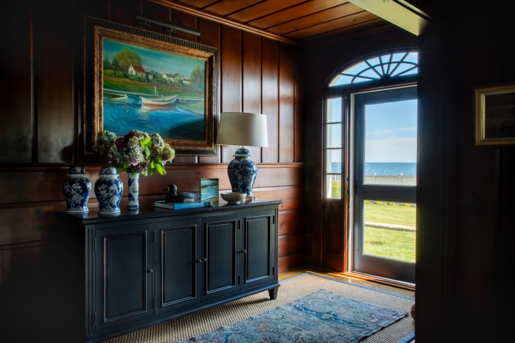 Entry hall vignette with nautical painting, blue chinoiserie vases, and wood paneling showcasing Newport’s rich residential design history.