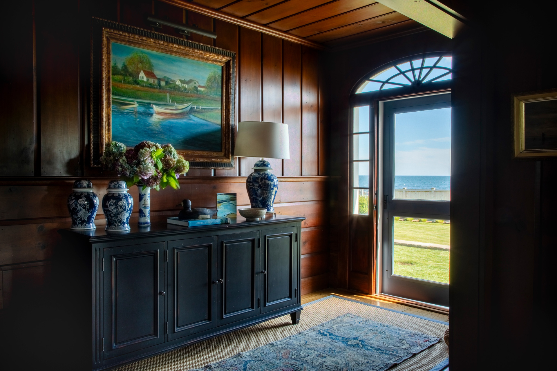 Entry hall vignette with nautical painting, blue chinoiserie vases, and wood paneling showcasing Newport’s rich residential design history.