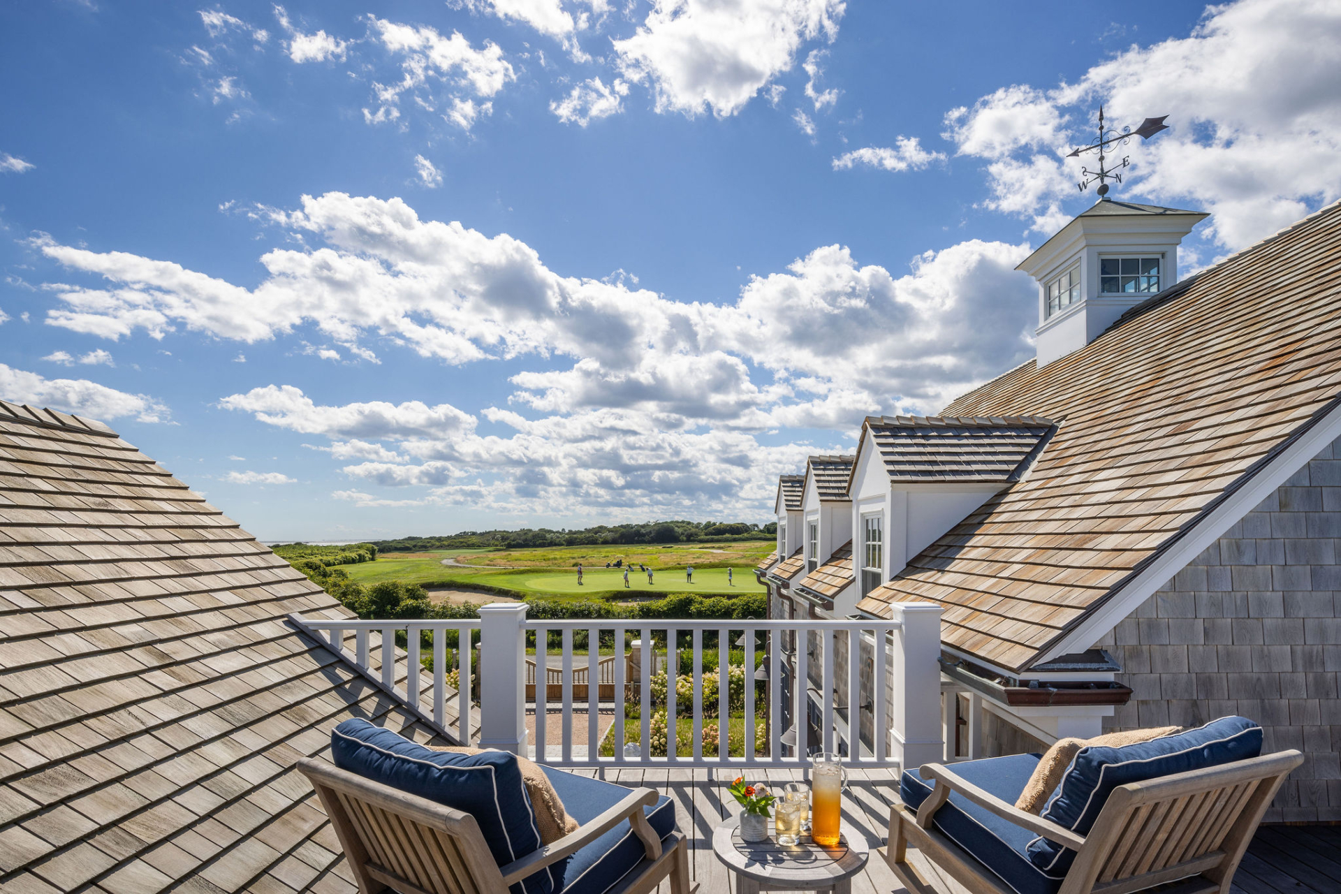 View from a second-story deck with navy lounge chairs overlooking a golf course and expansive sky with scattered clouds.