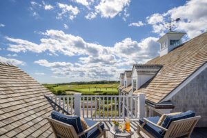 View from a second-story deck with navy lounge chairs overlooking a golf course and expansive sky with scattered clouds.