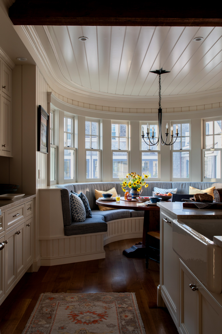 A breakfast nook in a coastal kitchen with a circular banquette and blue cushions.