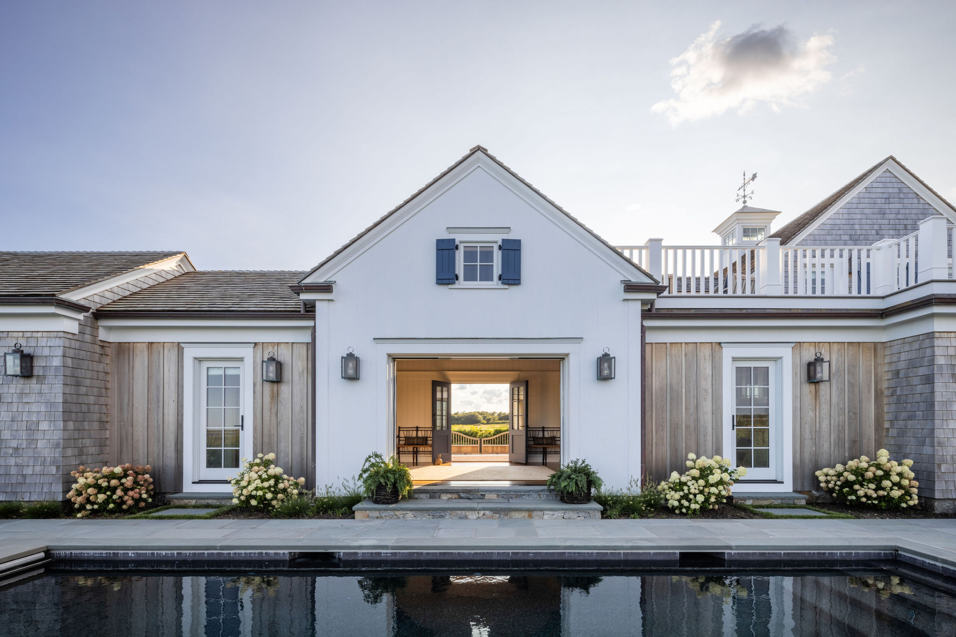 Ocean Lodge pool elevation with symmetrical white façades and barn doors opening to views, demonstrating seamless integration of original scale with coastal design updates.