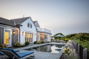 Serene poolside patio with striped lounge chairs, blooming hydrangeas, and coastal architecture lit in the soft glow of dusk.