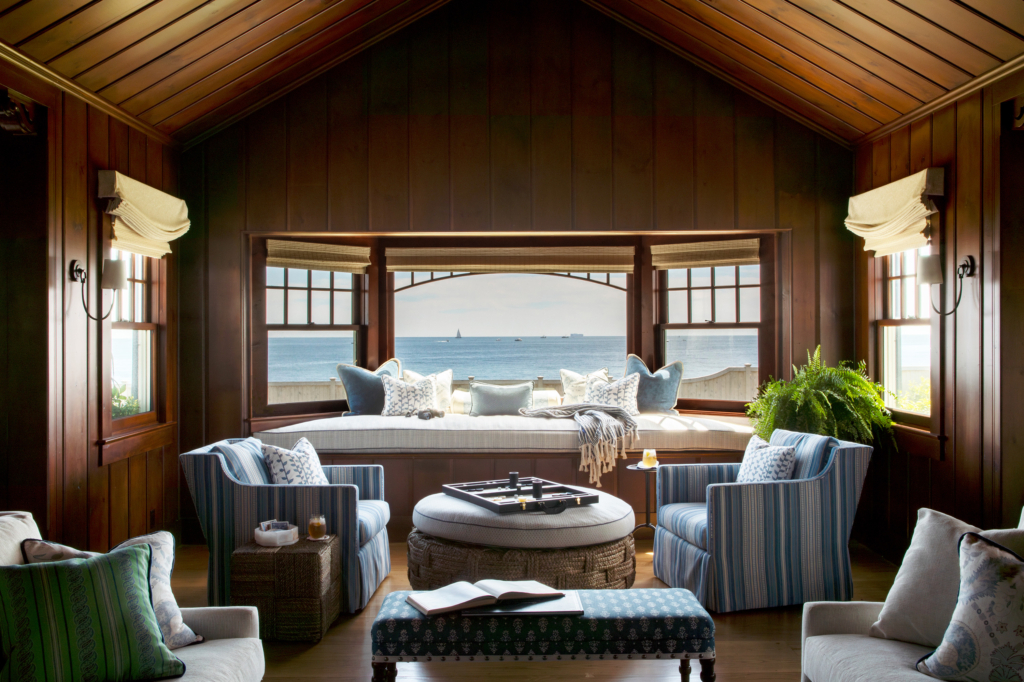 Ocean Lodge’s dramatic window seat with panoramic water views, custom cushions, and vintage-style furnishings surrounded by warm wood interiors.