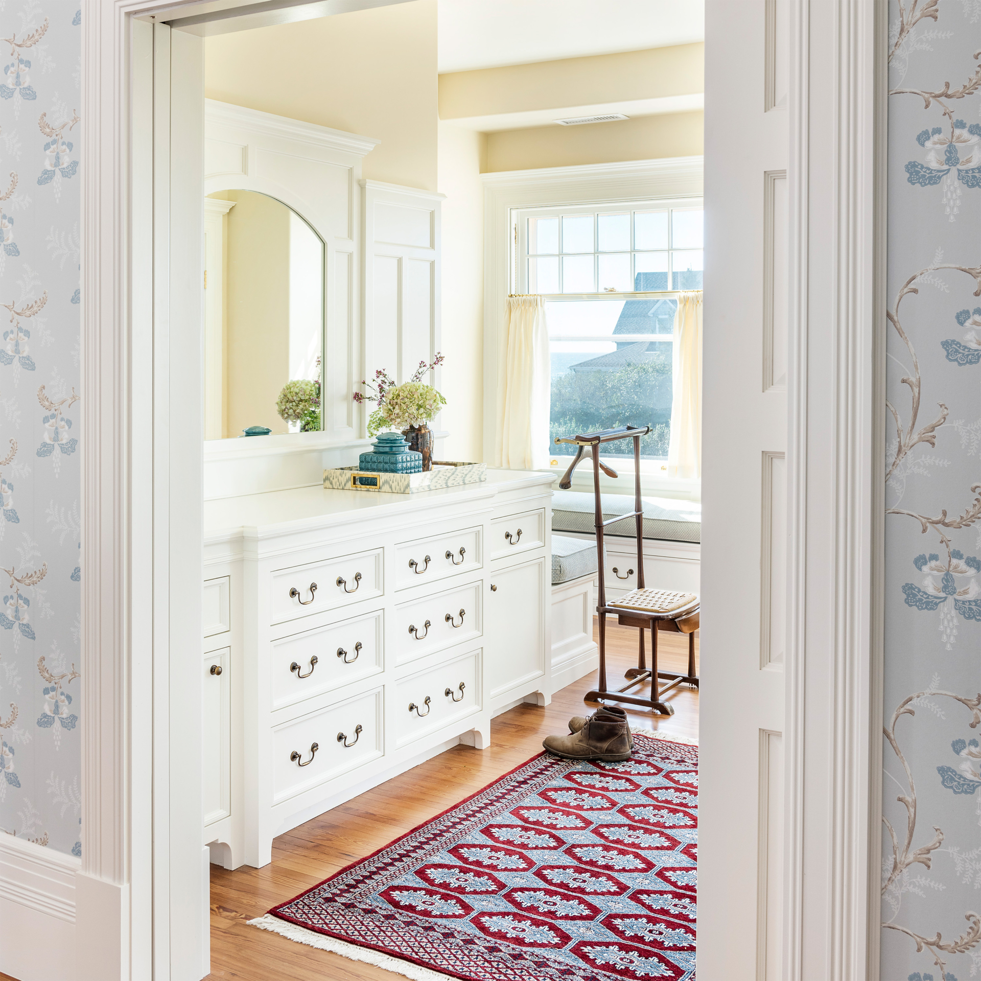 The primary closet with white built ins and red antique rug in the bedroom suite of Stone Lea, a historic McKim Mead and White home in Narragansett renovated by Taste Design.