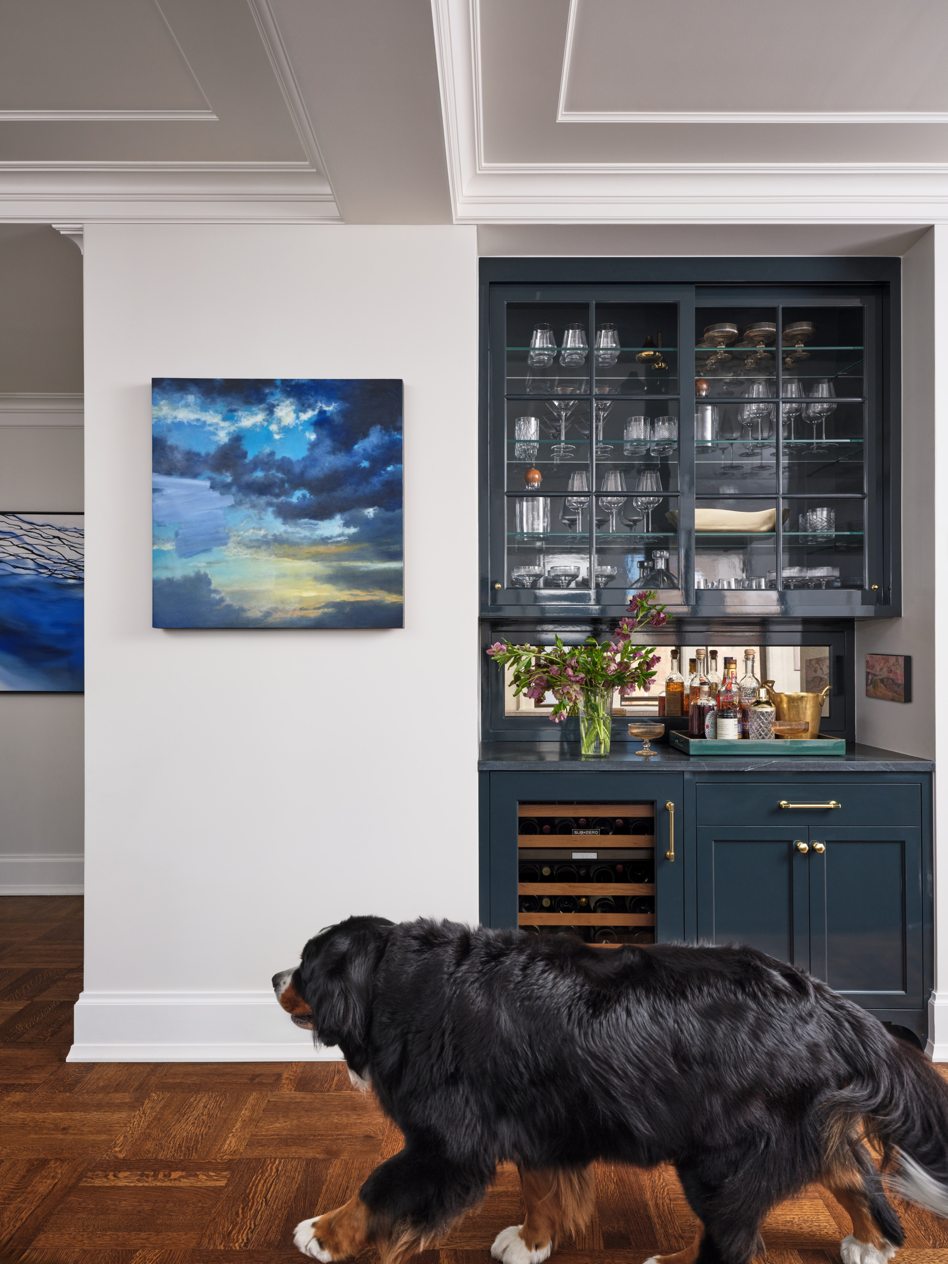Bernese Mountain Dog walking past home bar with navy cabinetry in Upper West Side apartment renovation.