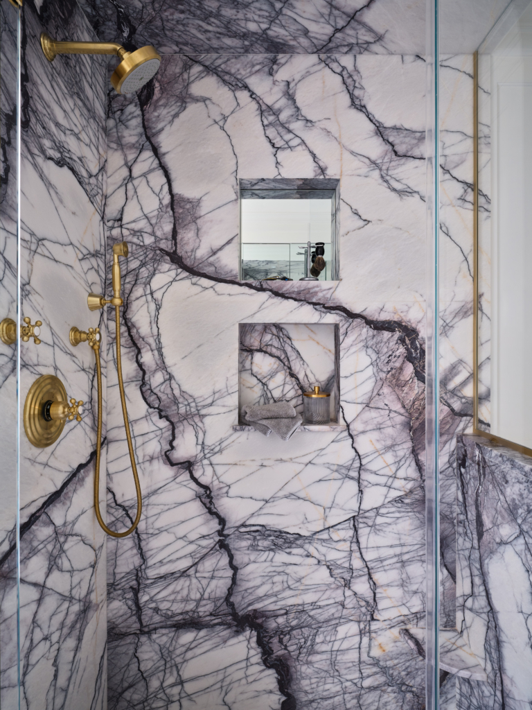 Shower with dramatic marble walls and brass fixtures in Upper West Side apartment renovation.