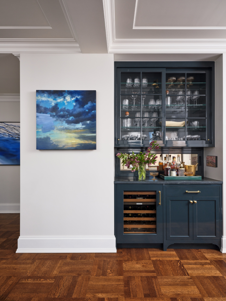 Home bar with navy cabinetry, brass hardware, and glass display in Upper West Side apartment renovation.