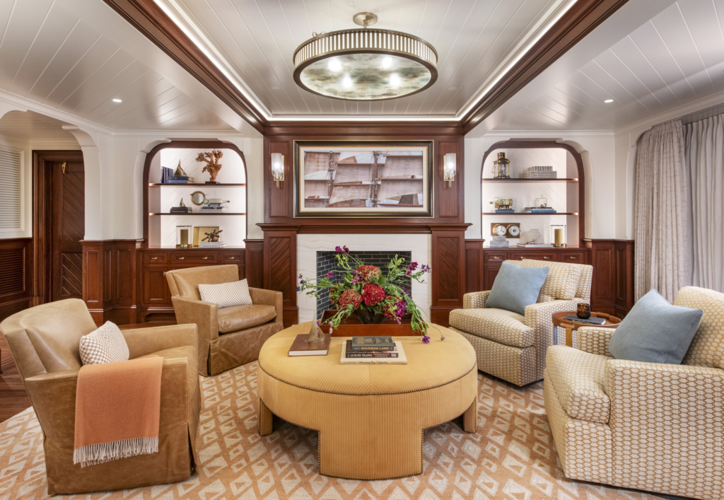 A buttery yellow and mahogany seating area with drop screen television over fireplace