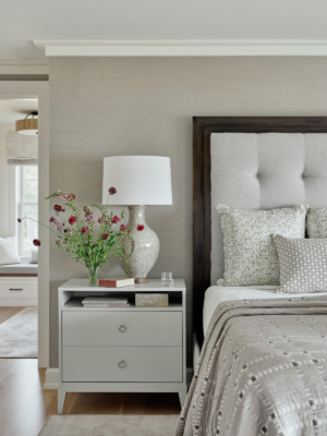 An upholstered bed with side table and flowers.