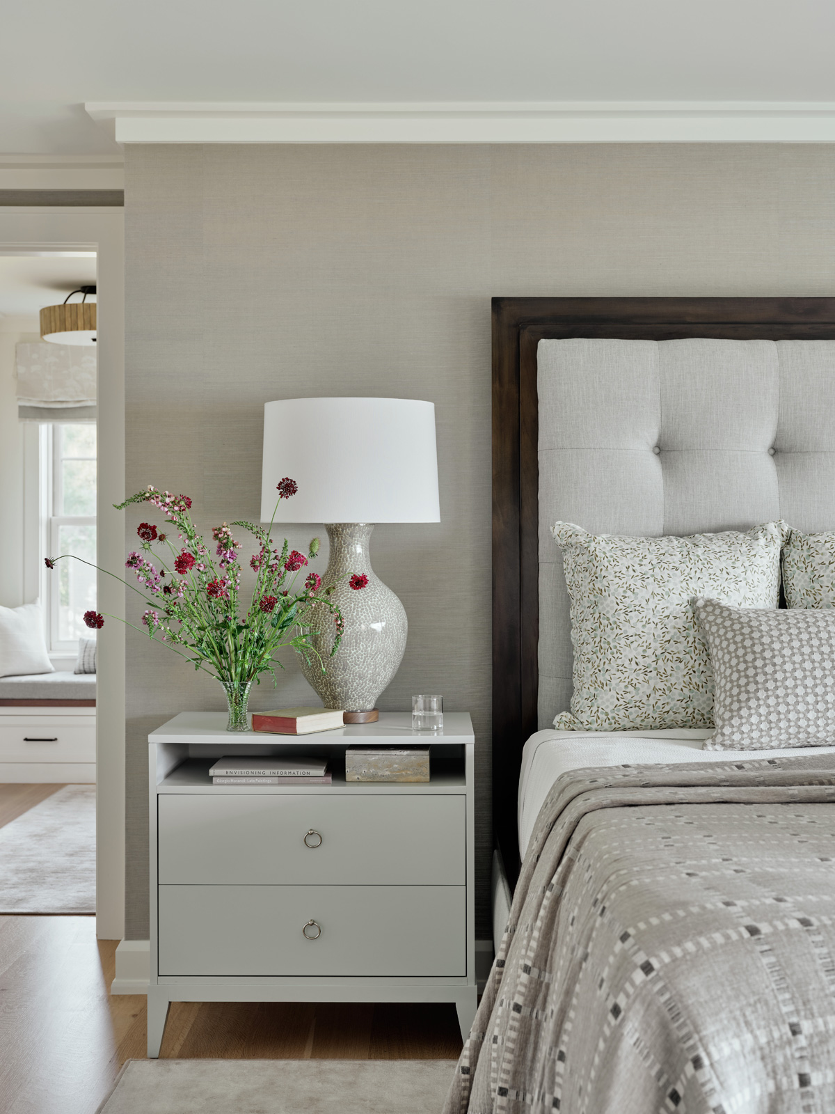An upholstered bed with side table and flowers.